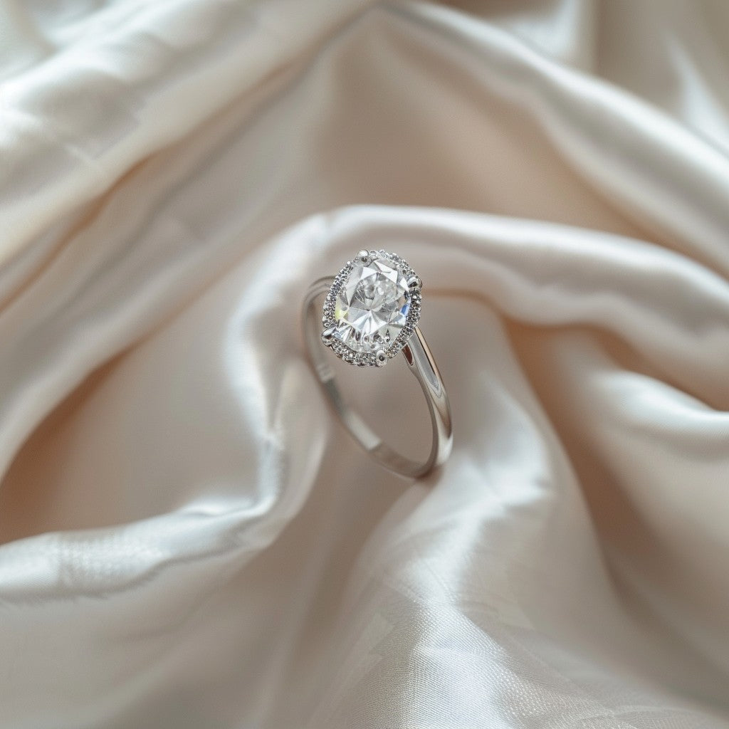 Nestled gently on a backdrop of soft, white silk, an elegant engagement ring captures the essence of sophistication and romance. 